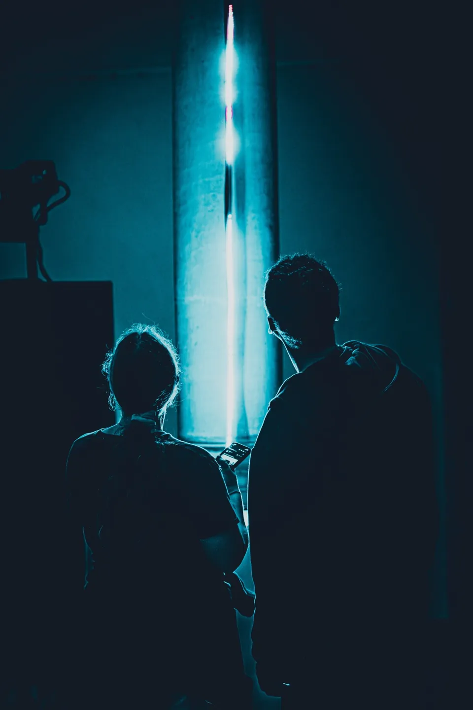 Zwei Silhouetten vor blauer Lichtsäule